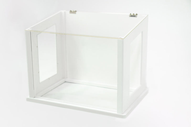 A white indoor dog potty with clear windows, silver hinges and sitting on a white floor.